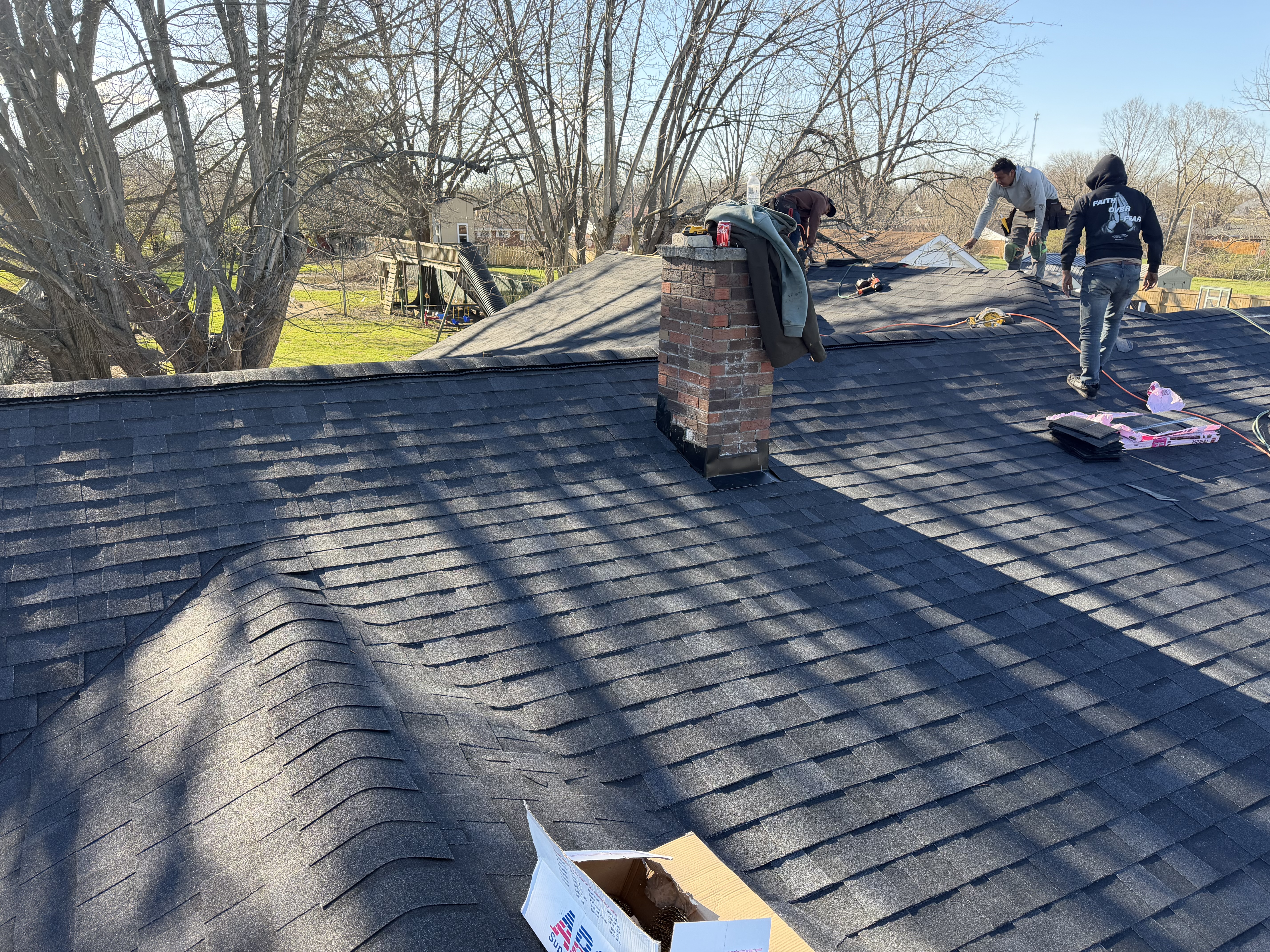 Roof crew working around a chimney and roof penetrations on an asphalt roof