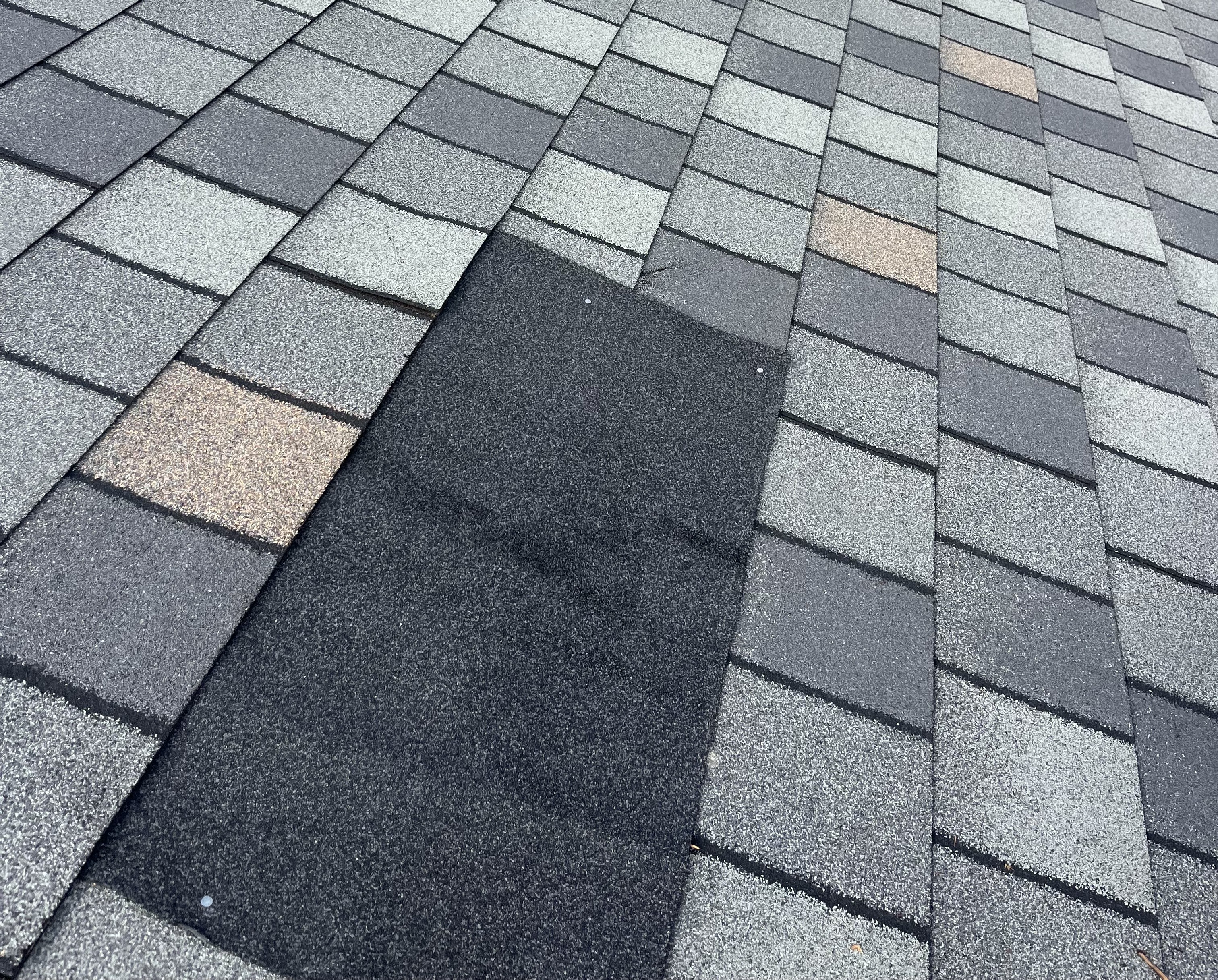 Close-up of asphalt shingles with a repaired section on a residential roof