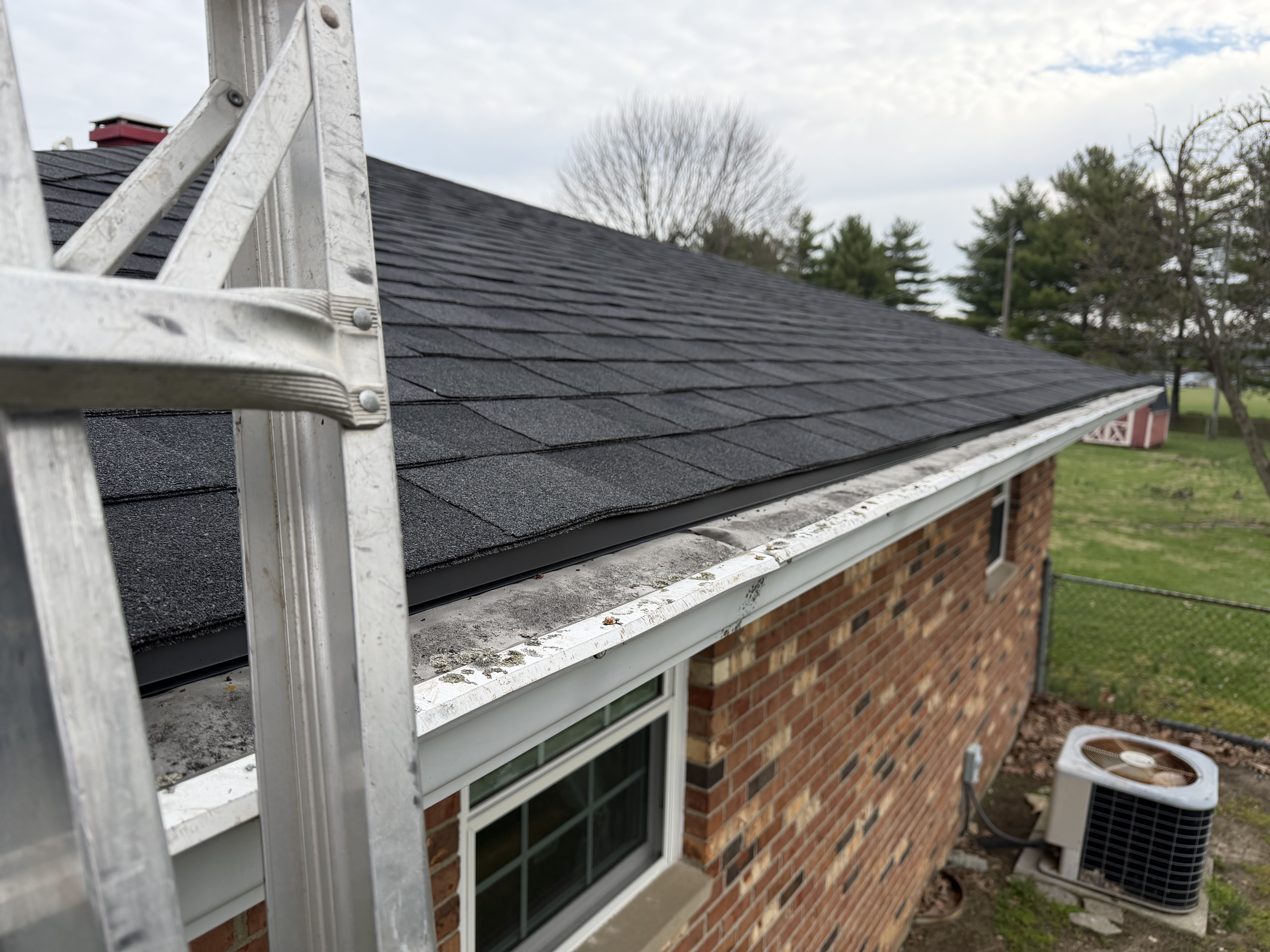 Gutter line being serviced from a ladder on a brick home