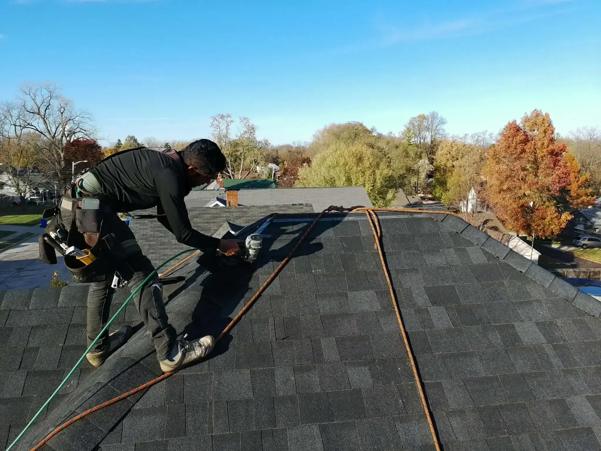 Roofer using a nail gun to install asphalt shingles on a residential roof