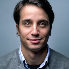 Man in a gray cardigan smiling against a blue background