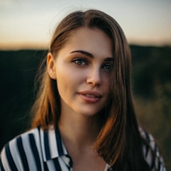 Woman with long brown hair in a striped shirt outdoors at sunset