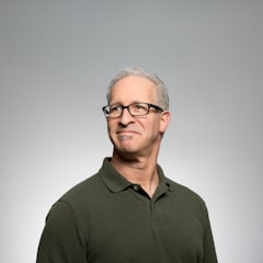 Man with glasses and gray hair wearing an olive green polo shirt